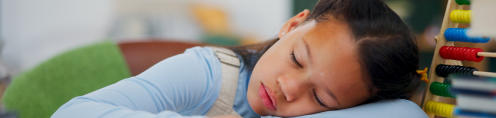 Kind schläft mit dem Kopf auf dem Tisch.