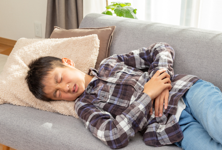 Kind liegt mit Bauchschmerzen auf der Couch.