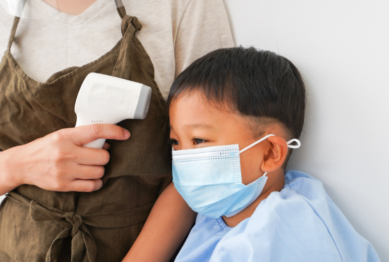 Kind mit Maske wird das Fieber gemessen.